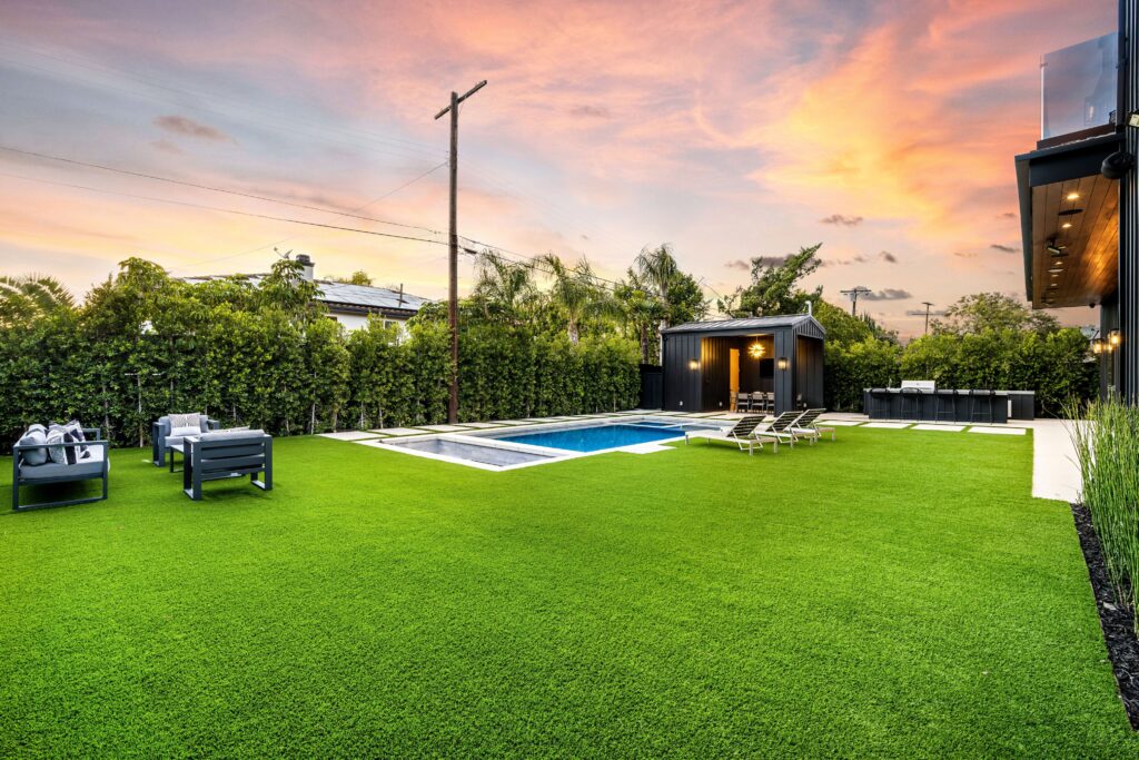 A luxurious backyard with a swimming pool, lounge chairs, and outdoor seating area at sunset.